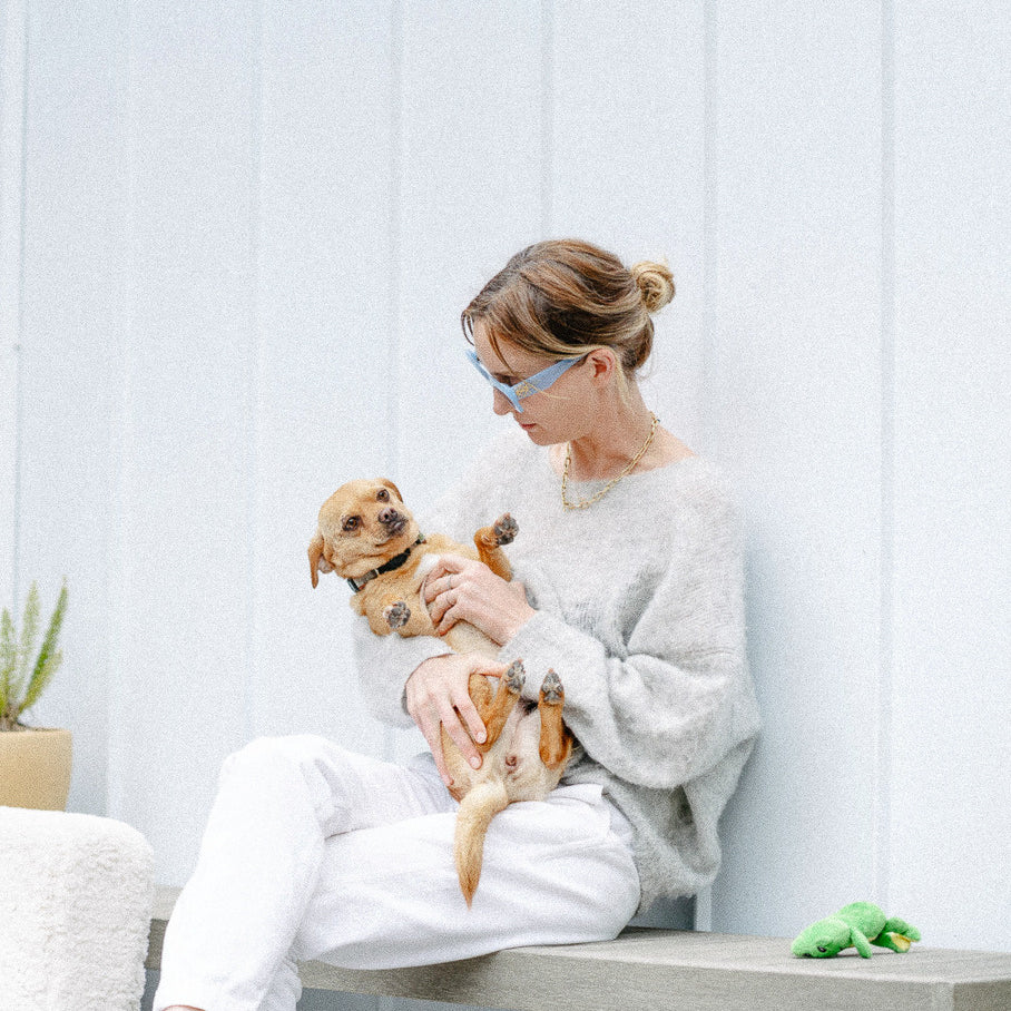 A woman wearing all gray holding her small, tan dog like a baby and giving him affection.