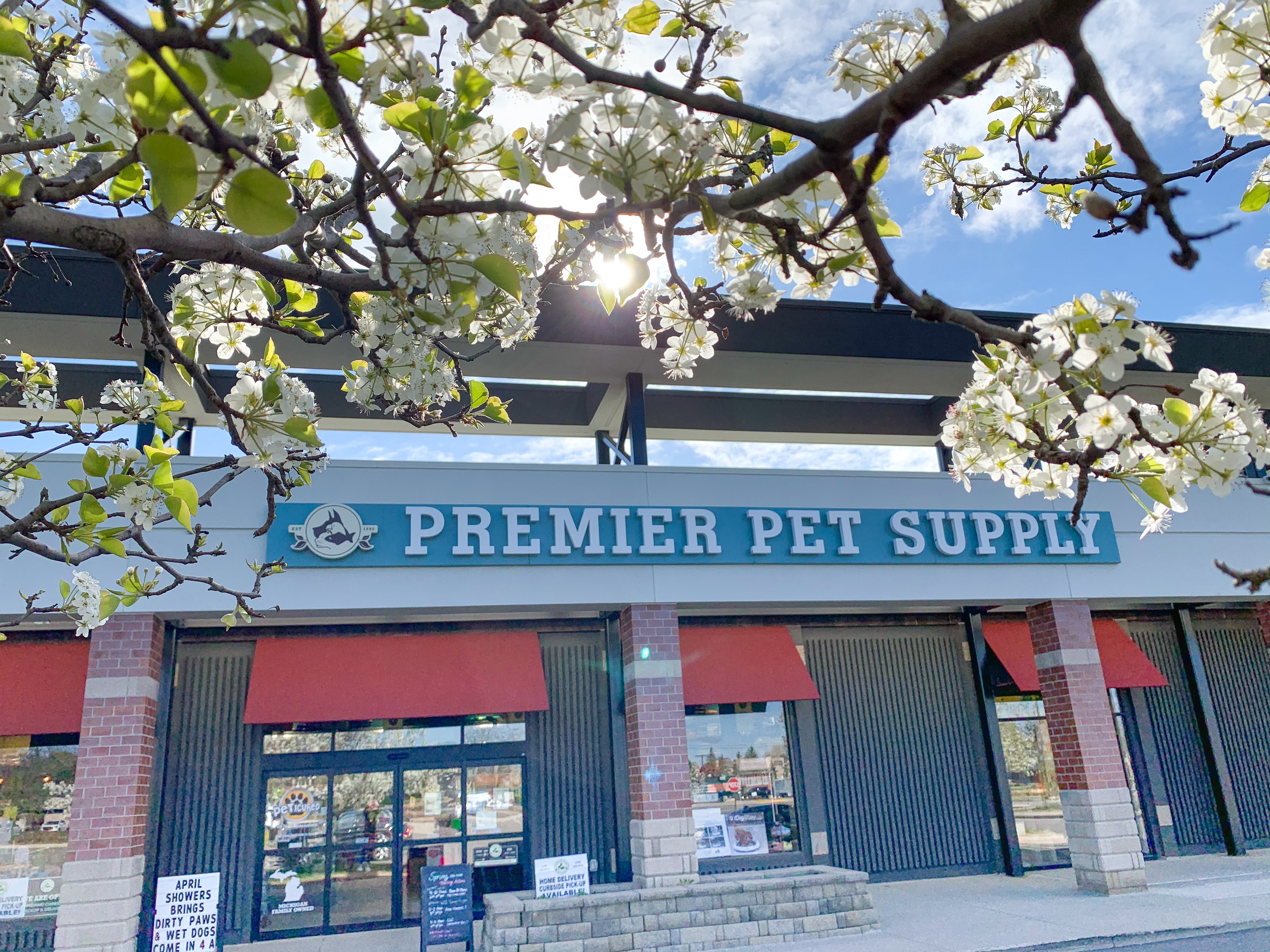 A bright image of the storefront for Premier Pet Supply against a blue sky. Branches of a flowering tree can be seen at the top of the photo. 